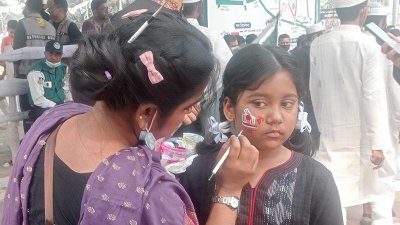 মুখে রঙ-তুলি দিয়ে একুশের বার্তা লিখে নিচ্ছে এক শিশু