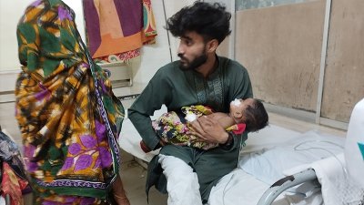 হামে আক্রান্ত শিশুকে কোলে নিয়ে বসে আছেন একজন তরুণ। ছবি: বাংলা ট্রিবিউন
