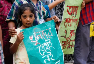 রামিসা হত্যার বিচার দাবিতে প্ল্যাকার্ড নিয়ে দাঁড়িয়ে আছে এক খুদে শিক্ষার্থী। ছবি: আহাদুল করিম খান