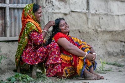 বাড়ির সামনে হাস্যোজ্জ্বল দুই আদিবাসী নারী। ছবি: উই ক্যান