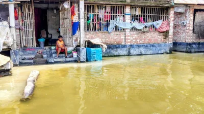 জলাবদ্ধ বাড়ির আঙিনায় বসে মাছ ধরছে ছোট্ট শিশু।