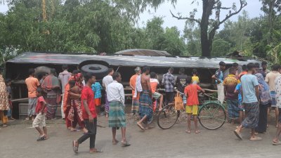 সড়কের পাশে বসতঘরের ওপর উল্টে পড়ে একটি বাস (ছবি: বাংলা ট্রিবিউন)